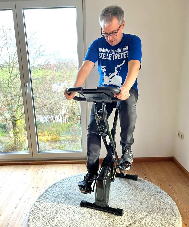Mann über 50 trainiert auf dem Tretmann Home im hellen Wohnzimmer
